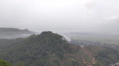 Puslu vadi manzarası, ormanlık tepeler, kıvrımlı nehir ve bulutlu gökyüzünün altındaki uzak yerleşim yerleri. Doğa, manzara veya seyahat temalı görsel içerik için ideal