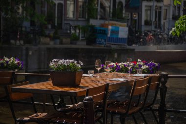 Kanal kenarında cam ve çiçeklerle süslü restoran masası Amsterdam, Hollanda sokakları.
