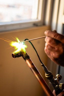 Bir işçi merkezi ısıtma için gaz lambası ile bakır borular kaynak yapar.