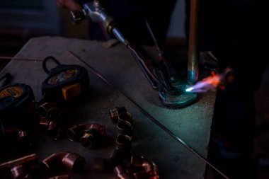 Bir işçi merkezi ısıtma için gaz lambası ile bakır borular kaynak yapar.
