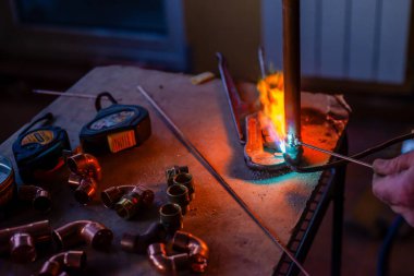 Bir işçi merkezi ısıtma için gaz lambası ile bakır borular kaynak yapar.