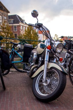 24.10.2024, Leiden, Hollanda, Leidens 'in tarihi merkezinin manzarası, kaldırım taşı caddesinde park edilmiş klasik bir motosiklet. Arka planda bisiklet ve klasik Hollanda mimarisi şehir cazibesine katkı sağlar.