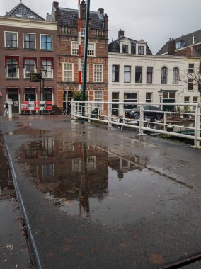 Leiden, Hollanda: Köprüdeki su birikintilerindeki tarihi binaların yansımasıyla Leiden 'da yağmurlu bir gün. Sahne, Hollanda mimarisinin cazibesini ve şehrin sakin atmosferini yakalıyor.