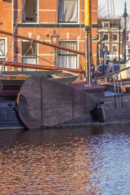 17.03.2025 Leiden, Hollanda. Hollanda, Leiden, Hollanda 'da tuğladan evler, yeşil budanmış pencereler ve parıldayan su yansımaları bulunan tarihi bir kanala demirlenmiş bir teknenin geleneksel ahşap dümenine yakın plan..