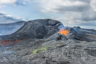 Reykjanes Yarımadası 'nın İzlanda manzarası. Volkanik kraterde gün boyunca az lav ve güneş var. Kraterin ağzından küçük lavlar akar. Kraterin etrafında karanlık ve soğuk magma var.