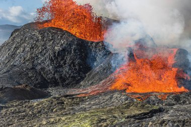 İzlanda 'daki lav çeşmeleriyle püsküren volkanın doğrudan görüntüsü. Gündüz aktif volkan. Volkan güçlü lav akışıyla patlıyor. Kraterin etrafındaki karanlık kayalar. Volkan kraterinden çıkan buhar.