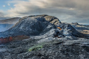 Patlamalar arasındaki günde aktif volkanik krater. Reykjanes yarımadasının İzlanda 'sındaki volkanik manzara. Kraterin etrafındaki soğutulmuş koyu magma kayaları. Gökyüzündeki bulutlar gün ışığında