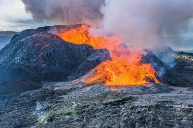 İzlanda 'da volkanik manzara. GeoPark 'taki Reykjanes Yarımadası' nda aktif volkan. Volkanik krater püskürme sırasında güçlü lav akışına sahiptir. Kraterin üzerinde yoğun dumanla parlayan lav.