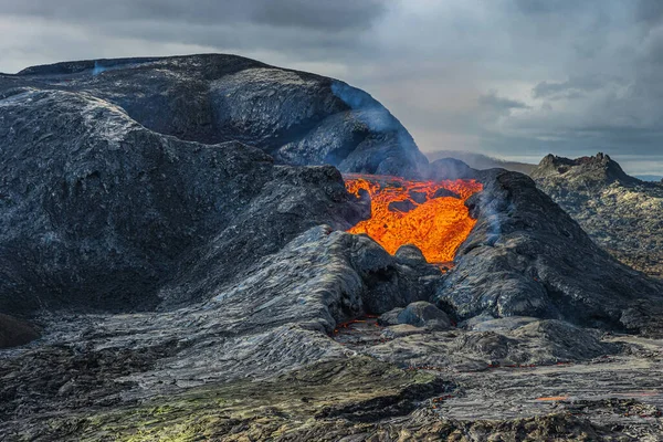 岩浆从火山口流出来 火山喷出的炽热的红色液体岩浆 冰岛雷克雅未斯半岛的火山景观 火山口周围是黑暗的 冷却的岩浆岩石 多云的天空 — 图库照片