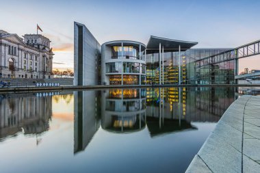 Berlin 'deki hükümet bölgesinde akşamları Spree nehri var. Reichstag ve Paul Lbe Evi gün batımında su yüzeyine yansıyor. Nehir kıyısında aydınlatılmış ev cephesi