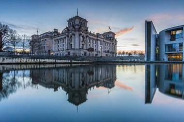 Berlin 'deki hükümet bölgesinde gün batımı. Reichstag, Almanya 'nın başkentinde. River Spree binanın önünde yansımalarla. Gökyüzünde hafif kırmızımsı bulutlar