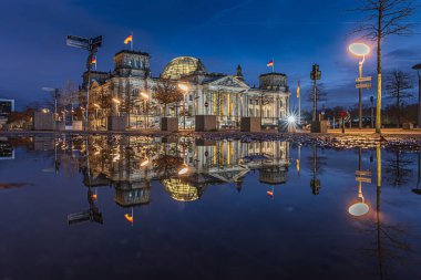 Berlin 'deki Reichstag' da, mavi saatte. Akşamları yanan binalar ve sokak lambaları. Su yüzeyindeki binanın yansıması. Almanya 'nın başkentinin kışında akşam havası