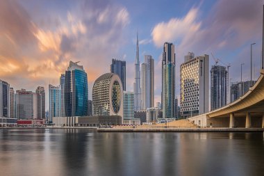 Dubai 'de gün batımında uzun pozlama. Burj Halife 'nin etrafında ofis binaları ve gökdelenleri olan bir iş merkezi. Finansal bölge bulutlu gökyüzü ile akşam ufuk çizgisi