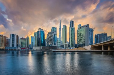 Akşamları Dubai siluetinin manzarası. Burj Halife ile birlikte şehrin Marina Körfezi 'nde gökdelenlerin üzerinde gün batımı. İş merkezi binası ve caddeleri olan bir köprünün parçası.