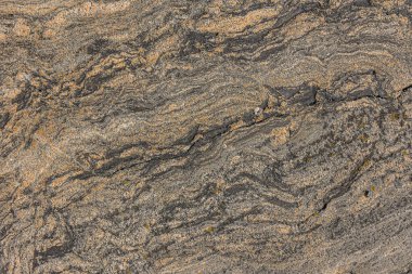 Dalgalı çizgileri ve küçük çizgileri olan granit bir yapı. Arka plan desenli, kahverengi eğimli doğal taş. Taştaki aydınlık ve karanlık noktalar hava şartlarından kaynaklanıyor.