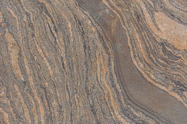 Kahverengi granit bir taşın dalgalı deseni. Arka plan desenli, kırık çizgileri olan doğal bir taş. Yüzeyde koyu renk kesintileri var. Çapraz dolambaçlı çizgi yapısı