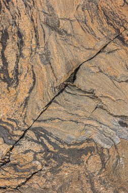 Kahverengi granit taşta kaba dalga deseni. Doğal taşın arka plan deseni. Yüzeyde çapraz yapısal bozulma. İzole edilmiş gri ve koyu bölgeler.