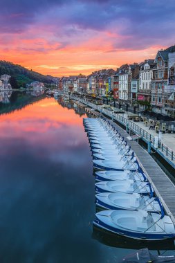 Dinant şehrinin Belçika 'sında renkli bir günbatımı. River Maas ve nehir kenarındaki eski evler. Evlerin yansıması ve su yüzeyinde gün batımı. İskeleye bağlı bir sürü tekne var.