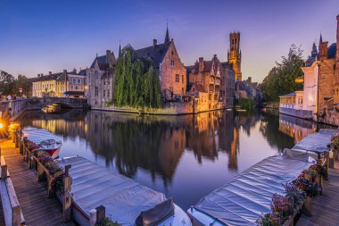 Akşam Bruges 'deki tespih rıhtımında. Kanal manzaralı, tarihi binalar ve ünlü çan kulesi. Su yüzeyindeki eski tüccar evlerinin yansımaları. İskelede tekneler