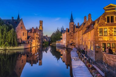 Rosary Quay in the Hanseatic city of Bruges. Reflection on the water surface of the canal of the historic buildings in the evening. Belfry tower of the old town and historic guild houses clipart