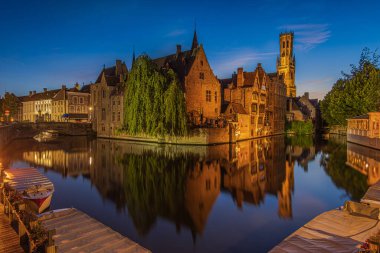 Rosary Quay at the evening in Bruges. Center of the old Hanseatic city with canal at blue hour. Reflections of illuminated historic merchant houses and belfry on the water surface clipart