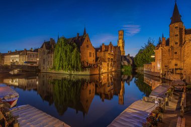 Center of the old town of Bruges with a view of the Rosary Quay. Old Belgian Hanseatic town with canal at blue hour. Reflections of illuminated historic merchant houses and belfry on the water surface clipart