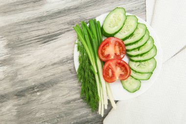 Sliced vegetables cucumbers, tomatoes and greens on a white plate top view
