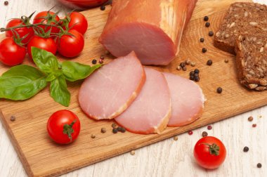 Ham on a wooden board decorated with tomatoes and basil