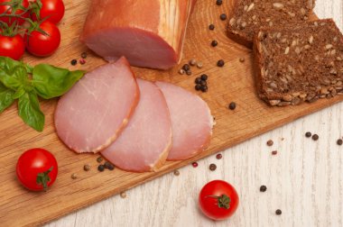 Ham on a wooden board decorated with tomatoes and basil