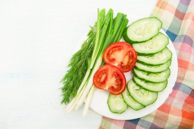 Sliced vegetables cucumbers, tomatoes and greens on a white plate top view