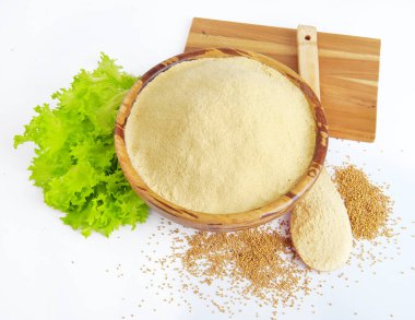 Mustard powder in a bowl, lettuce leaves and a wooden spoon on a white background