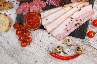 Ketçap ve domatesli grafit tahtasında farklı sosis ve domuz yağı çeşitleri.