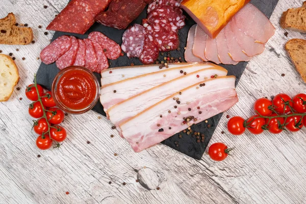 Stock image Antipasti different types of sausages and lard on a graphite board with ketchup and tomatoes.Top view