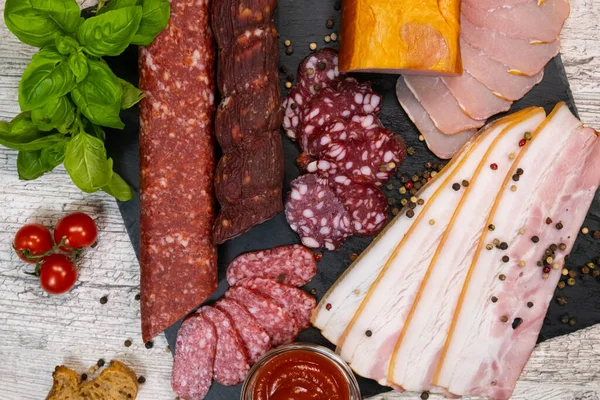 stock image Antipasti different types of sausages and lard on a graphite board with ketchup and tomatoes.Top view