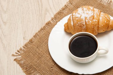 Tabakta bir fincan kahve ve peçetede bir kruvasan.