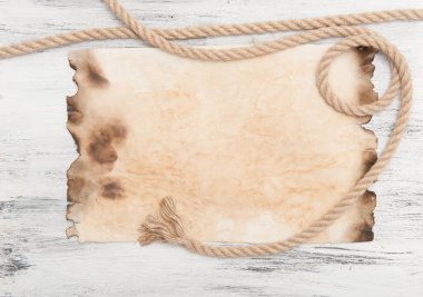 Kenarlarında yanık parşömen olan kolaj ve ahşap bir tahta üzerinde ip.