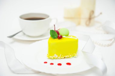 Bir fincan kahve, kalp şeklinde kek, sarı jöleli, beyaz arka plandaki bir tabakta.