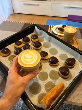 Glass of cappuccino in a man hand over a baking sheet with custard cakes with craquelins. High quality photo
