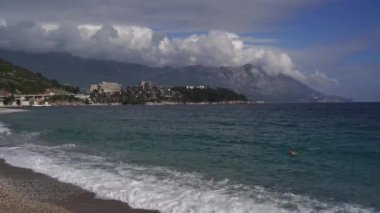 Sea waves roll on the shore against the backdrop of mountains and a cloudy sky. High quality 4k footage