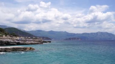 Stone breakwaters near the beach with sun umbrellas against the backdrop of mountains. High quality 4k footage