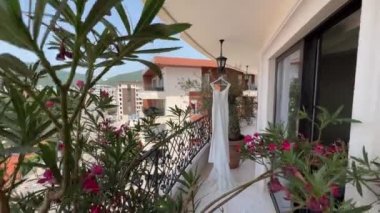 Flowering oleander in a pot stands on the hotel terrace with a white wedding dress on a hanger. High quality 4k footage