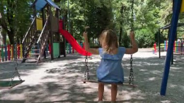 Küçük kız parkta salıncakta sallanıyor. Arkadan bak. Yüksek kalite 4k görüntü