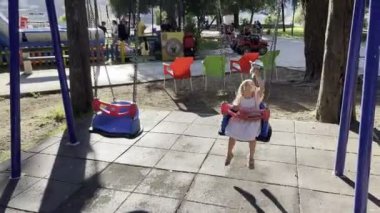 Little girl with a soft toy in her hand swings on a chain swing on the playground. High quality 4k footage