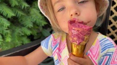 Little girl with a dirty face eats popsicles in a waffle cone. High quality 4k footage