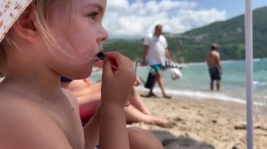 Little girl sits on the beach in a panama hat and eats grapes. High quality 4k footage