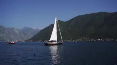 Birds fly around a small sailing yacht moored in the sea against the backdrop of mountains. High quality FullHD footage