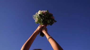 Bouquet of flowers in the hands of the bride against a bright blue sky. Cropped. High quality FullHD footage