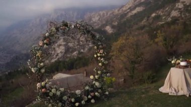 Yuvarlak düğün kemeri bir dağın tepesinde, bir masanın yanında duruyor. Yüksek kaliteli FullHD görüntüler