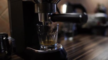 Coffee drips into a glass on a tray of a carob coffee machine standing on a table. High quality 4k footage
