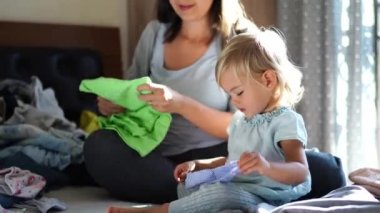 Little girl puts on a protective mask while sitting next to her mother sorting clean linen on the bed. High quality 4k footage
